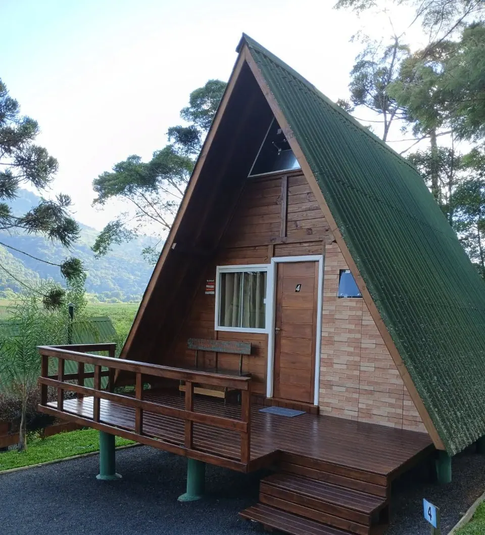 Chalé maior em A, de madeira e tijolinho, com telhado verde, porta nº 4 e varanda com escada