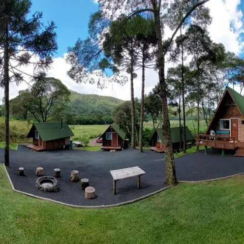 Panorama da propriedade: os chalés ao redor do pátio com a roda de fogueira, entre araucárias
