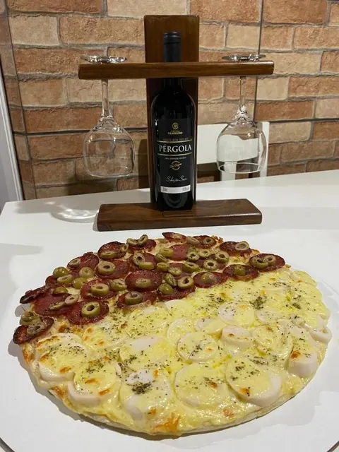 Pizza sobre a mesa, com uma garrafa de vinho e duas taças ao fundo